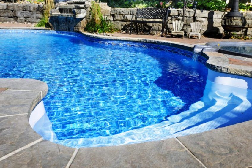 Residential inground swimming pool in backyard with waterfall and hot tub
